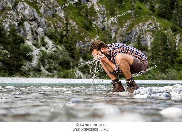 Hiker crouching at riverside washing his face