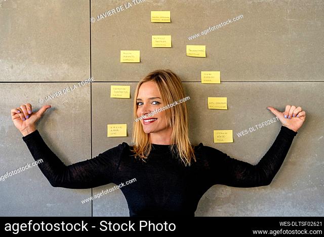 Businesswoman pointing at adhesive notes pasted on gray wall