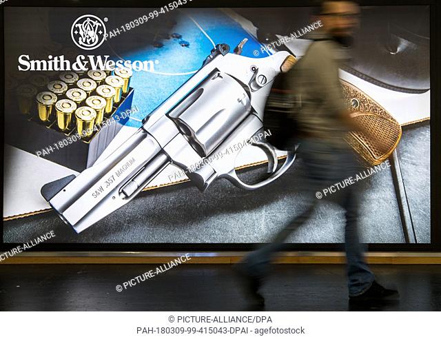 09 March 2018, Germany, Nuremberg: A visitor passes a poster by the American manufacturer Smith & Wesson (S&W) at the IWA OutdoorClassics trade show for hunting