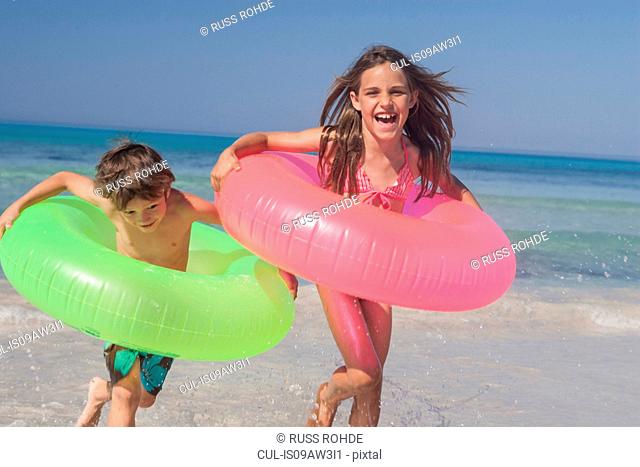 Girl and brother running on beach with inflatable rings, Majorca, Spain