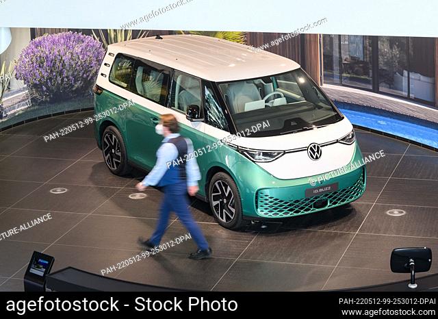 11 May 2022, Lower Saxony, Wolfsburg: An employee walks next to a Volkswagen ID.Buzz electric bus in the Autostadt at Volkswagen's main plant