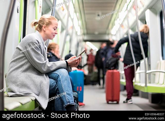 Beautiful blonde caucasian woman wearing winter coat reading on the phone while traveling by metro. Public transportation concept