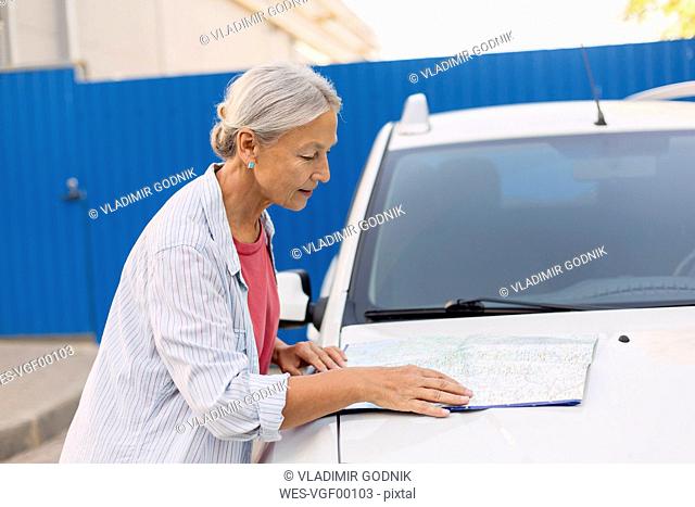 Senior woman looking at road map on her car bonnet