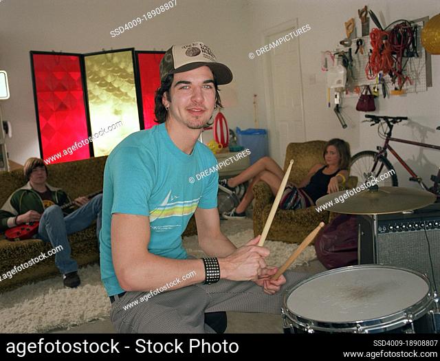 portrait of young garage band drummer practicing with friends in background