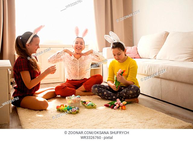 Girlfriends in bunny ears sitting on the floor and playing with Easter rabbit. The concept of preparation for Holiday