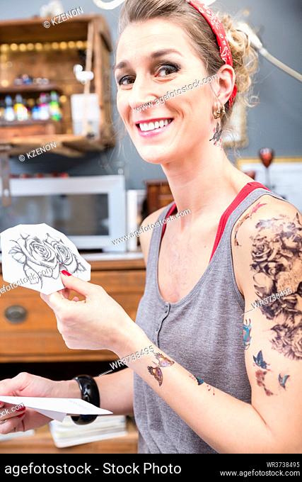 Portrait of a fashionable and beautiful woman looking at camera with a happy facial expression for choosing two roses as design for her new tattoo
