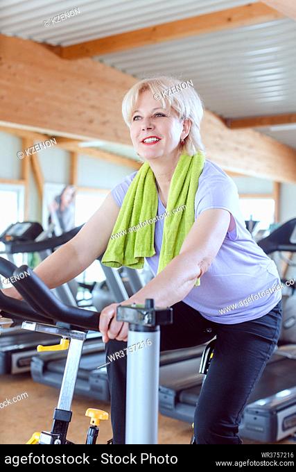 Senior woman exercising for better fitness on a bike in a modern gym