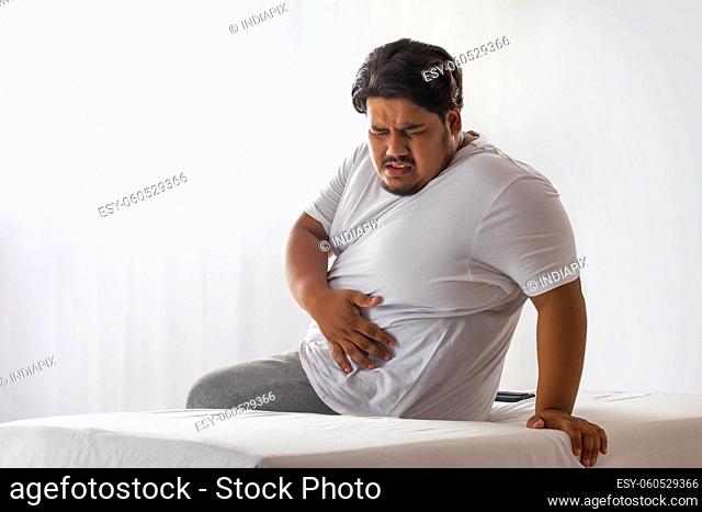 A fat man sitting and holding his belly in pain