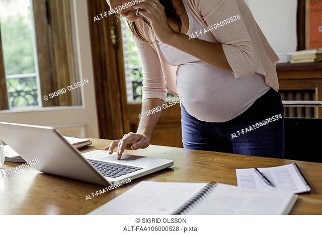 Pregnant woman using laptop computer and making phone call