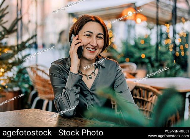 Happy mature woman talking on smart phone at sidewalk cafe