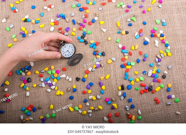 Pocket watch amid colorful pebbles on canvas background