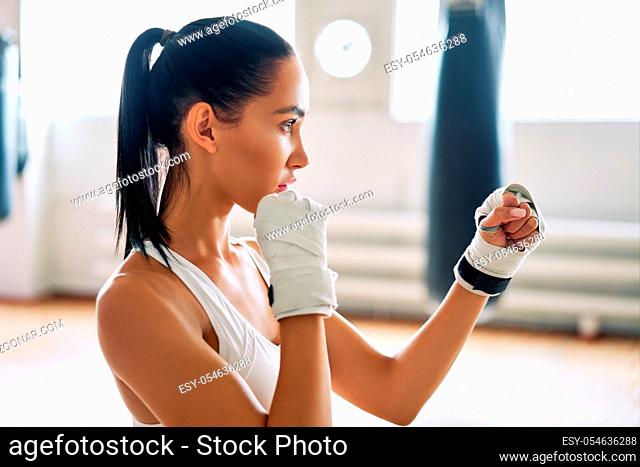 Young boxer woman posing in combat stance in gym. Sporty female ready for fight