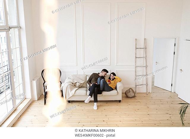 Couple sitting on the couch in the living room of new home looking at cell phone