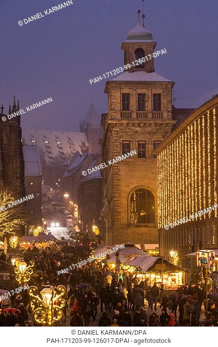 Visitors walk across the Christkindlesmarkt during snowfall in Nuremberg, Germany, 03 December 2017. Photo: Daniel Karmann/dpa