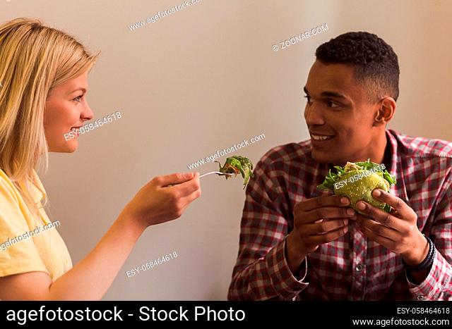 Happy couple spending free time in vegan restaurant or cafe. Lady feeding her boy-friend with vegan salad. Vegan concept