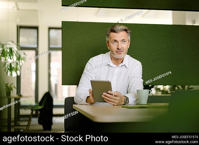 Businessman using digital tablet while sitting by table at cafeteria