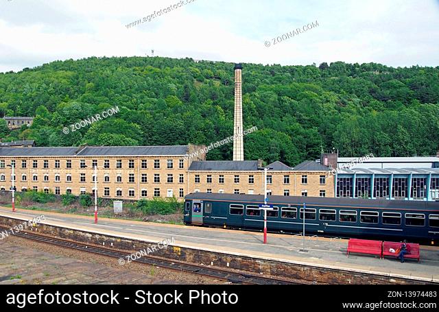 halifax, west yorkshire, united kingdom - 31 may 2019: a pacer train pulling into halifax railway station in west yorkshire with surrounding buildings and tree...