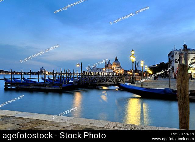 Beautiful image captured during the blue hour in Venice, foreground we see the typical Venetian Gondolas moored at the pier