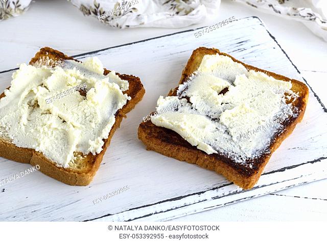 toasted bread with soft curd on a white wooden board, top view