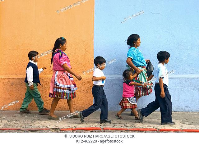 Mayan woman and children walking in front a painted wall. Antigua Guatemala. Sacatepéquez Region. Guatemala