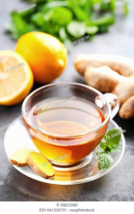 Cup of tea with ginger root and lemon on grey wooden table