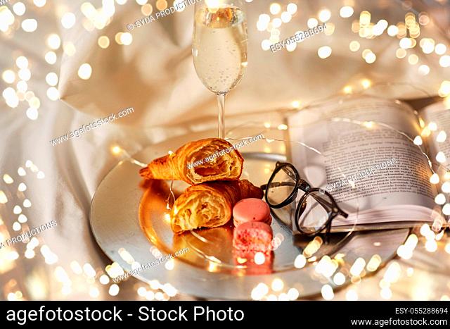 champagne, croissants, book and glasses in bed