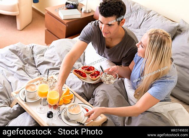 Married couple enjoying breakfast in bed with a healthy spread of jam on toast, fresh oranges and juice and a cup of coffee, high angle view