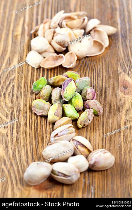 a bunch of salted roasted pistachios without a shell, lies on a wooden table, closeup of the first meal