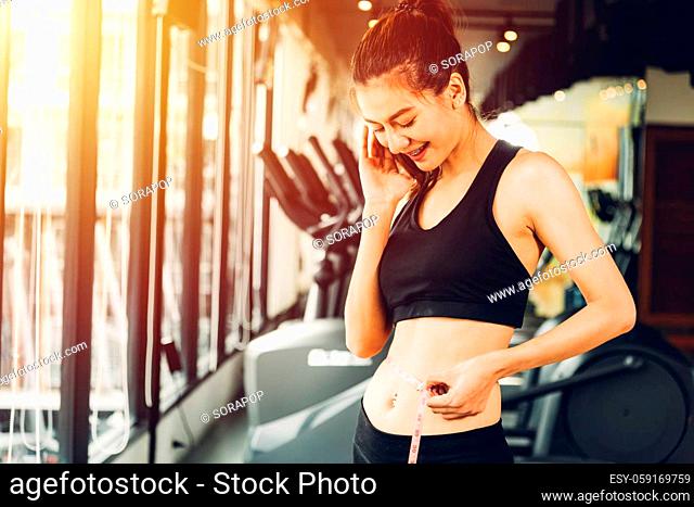 Happy asian beautiful woman have body shape slim by centimeter tape at fitness gym