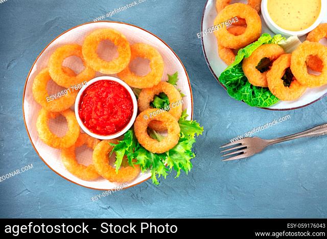 Calamari rings. Deep fried squid rings with lettuce and various sauces, overhead flat lay shot on a blue background