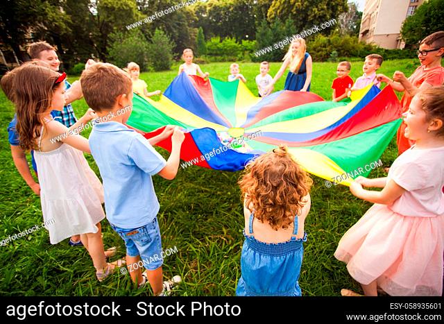 Happy kids holding parachute during funny game at summer park