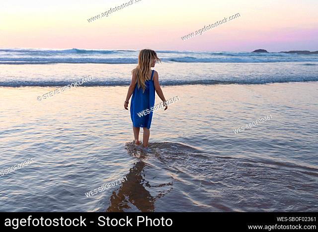 Girl in blue dress looking at view while walking at beach during sunset