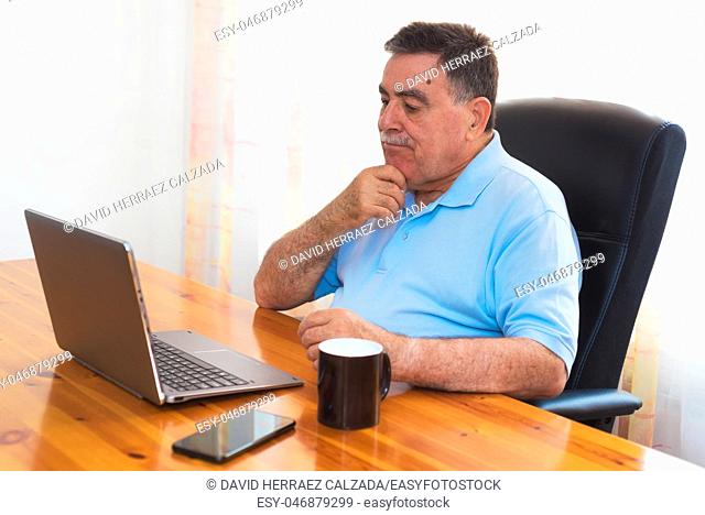 Senior man using laptop, doubtful expression. E-learning concept