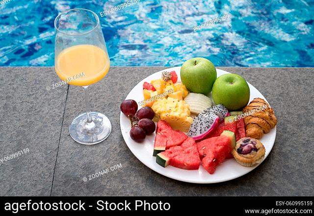 Fruit plate and glass of orange juice by hotel pool. Exotic summer diet. Tropical beach lifestyle