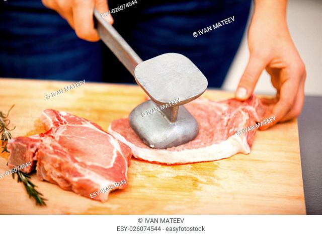 Young woman beating a steak in the kitchen