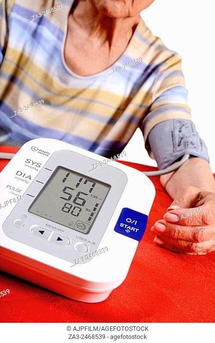 Home blood pressure testing. Elderly lady using a digital blood pressure monitor (sphygmomanometer) at home