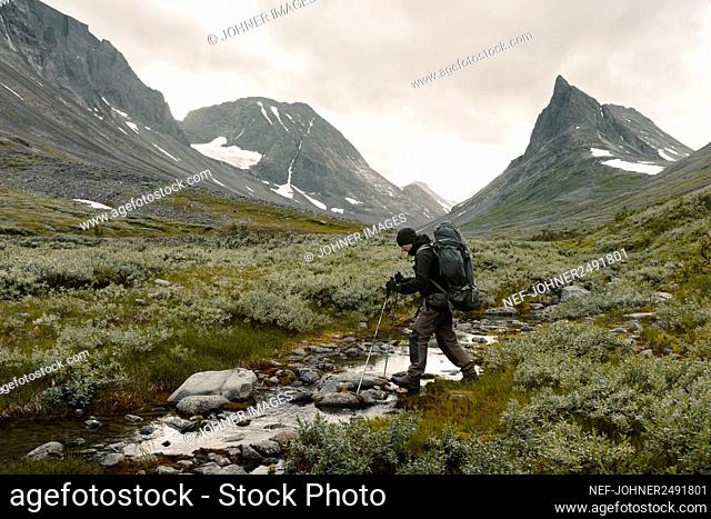 Hiker crossing stream in mountains