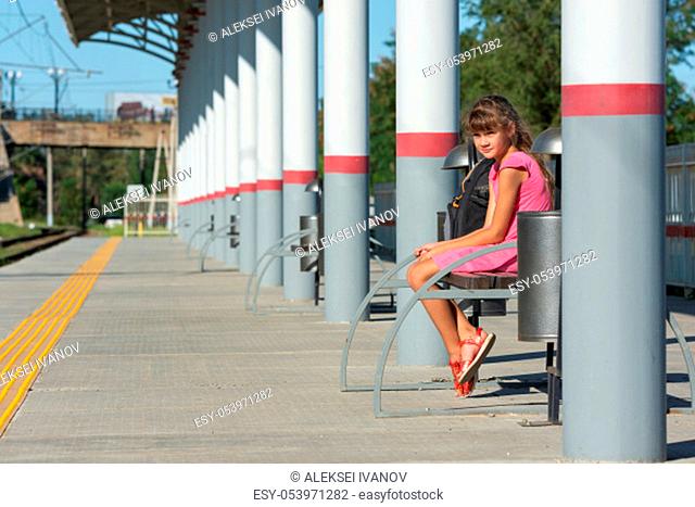 Eight-year-old girl sits alone on the empty platform of the train station
