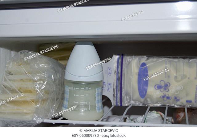 lot of frozzen breast milk in storage bags stored in the freezer and baby bottle with fresh expresed breastmilk, smille, breastfeeding concept