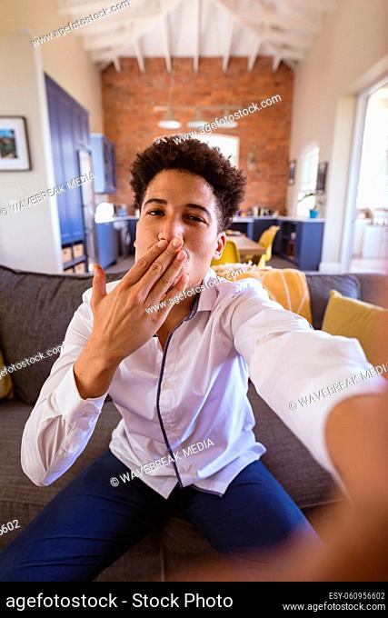 Portrait of biracial young man blowing air kiss on virtuality date at home