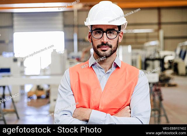Confident engineer wearing eyeglasses and protective workwear standing with arms crossed in industry