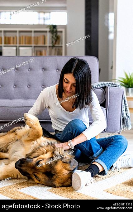 Playful young woman playing with pet dog while sitting on carpet at home