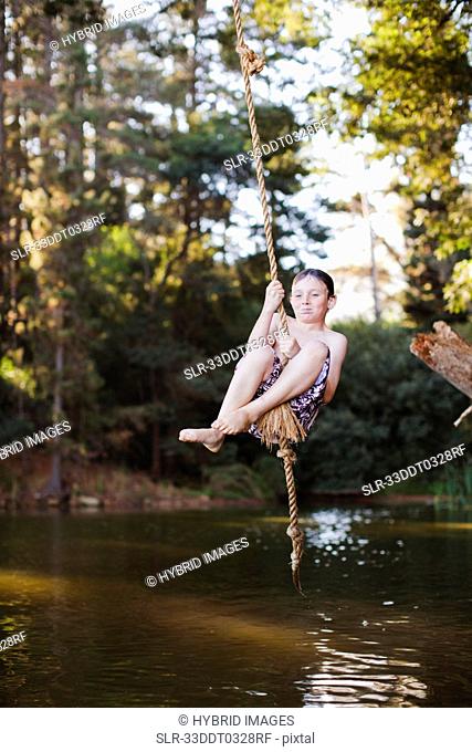 Young boy using rope swing over lake
