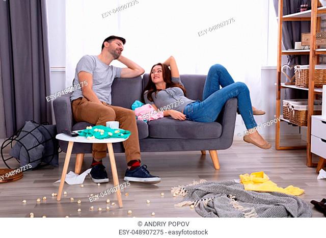 Smiling Couple Relaxing On Sofa In Messy Living Room At Home