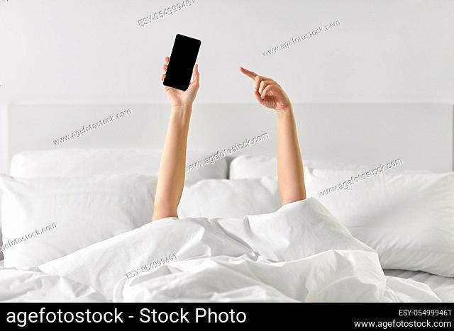 hands of woman lying in bed with smartphone
