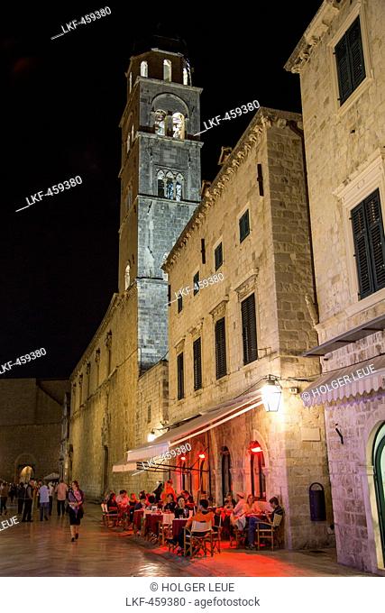People sitting outside a restaurant in the old town Placa with Franciscan Church monastery tower at night, Dubrovnik, Dubrovnik-Neretva, Croatia