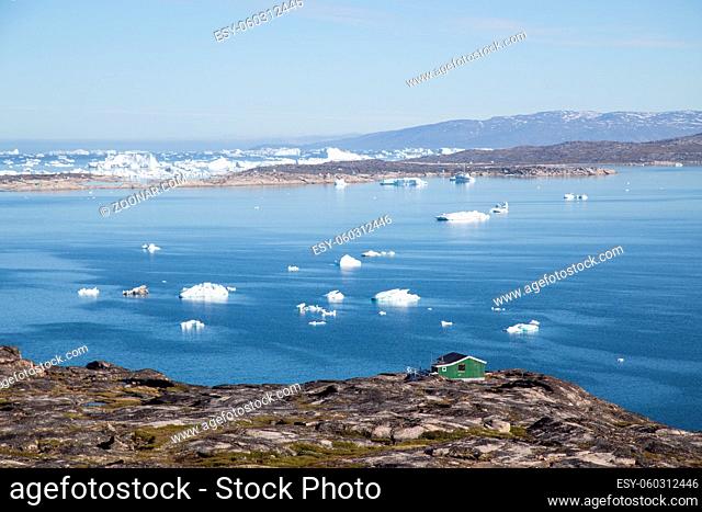 Ilulissat, Greenland - July 08, 2018: A green wooden house at the coast with icebergs in the background