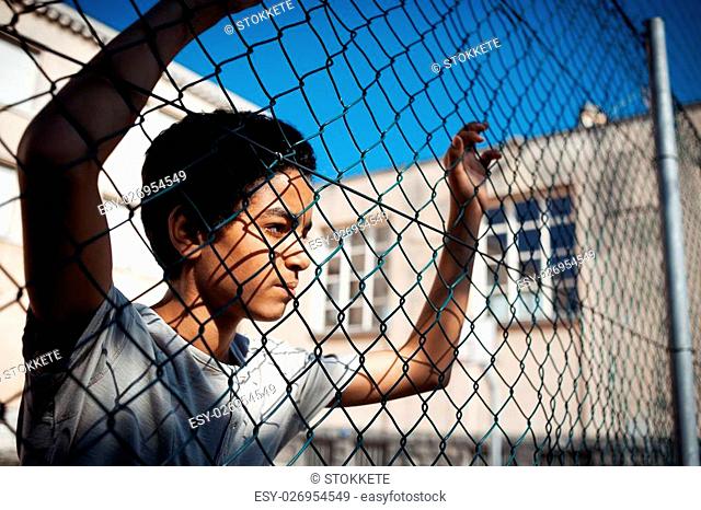 A boy looks while leaning up against a chain link fence
