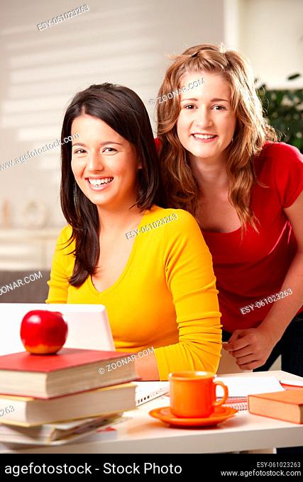 Teens learning at home with laptop computer and books looking at camera smiling