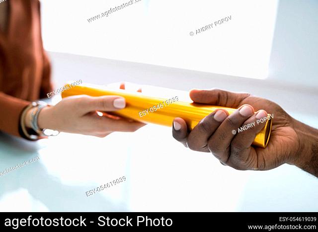 Close-up Of Businessman's Hand Passing The Golden Baton To His Partner In Office